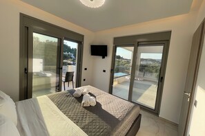 A hotel room with a bed, a TV, and a balcony with a view. - Nastazia's Pearl Villa (Afantou)