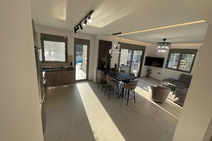 Une cuisine moderne dotée d’un grand îlot central, un coin repas avec une table et des chaises, et un espace de vie comprenant un canapé et un téléviseur.