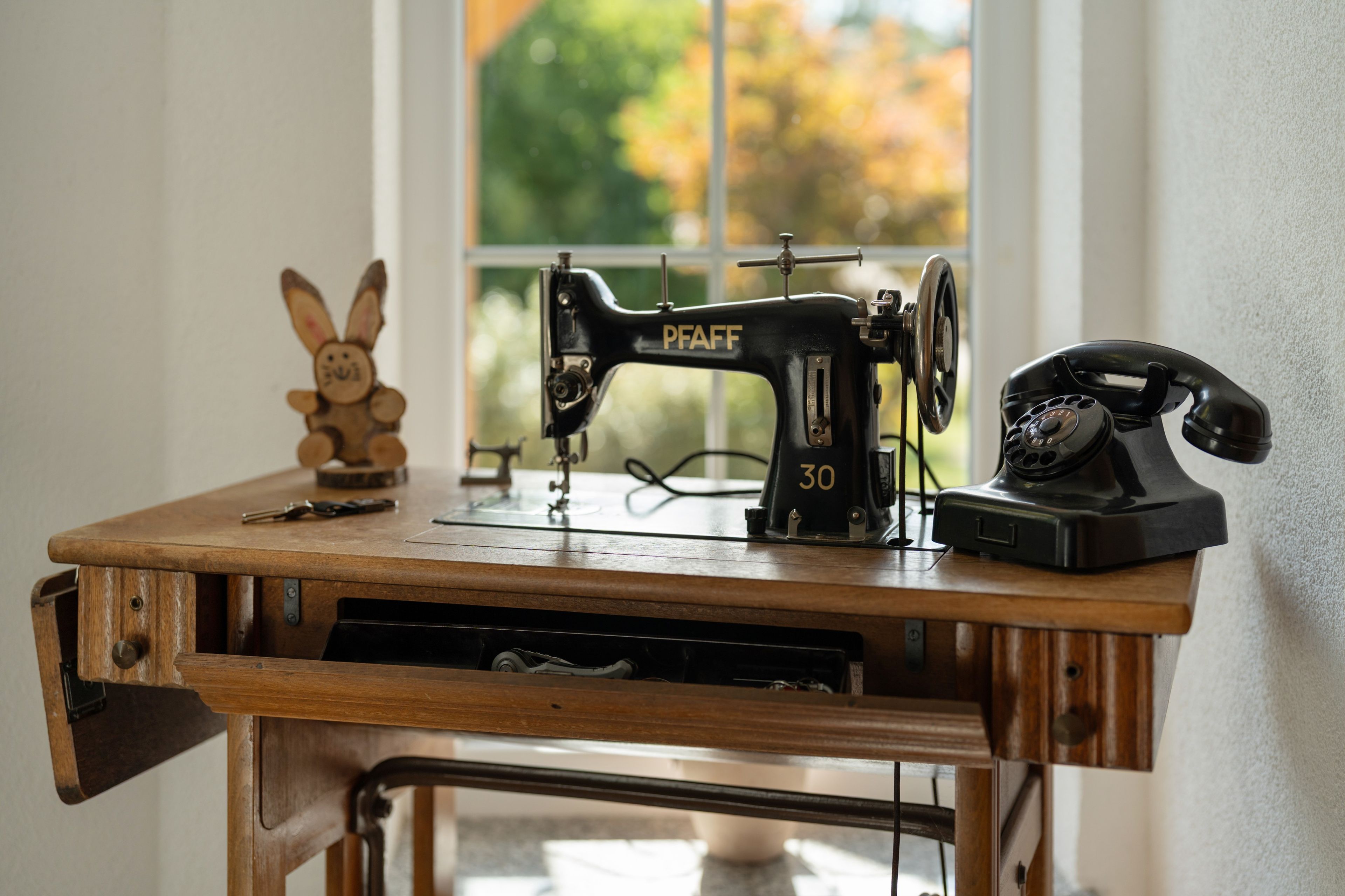 A sewing machine on a wooden table with a window in the background.
