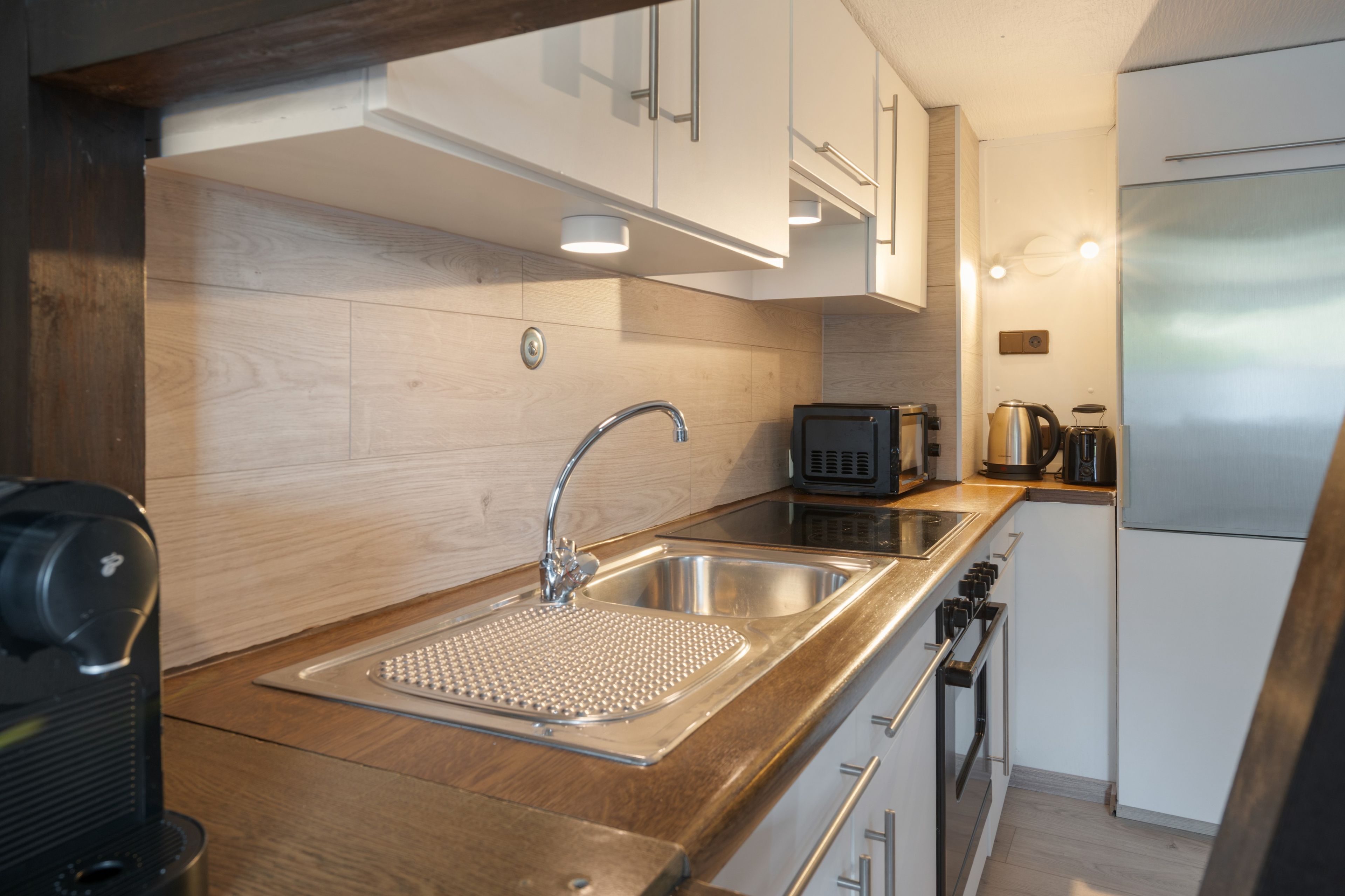 Una cocina moderna con un lavamanos de acero inoxidable, un horno empotrado y un microondas.