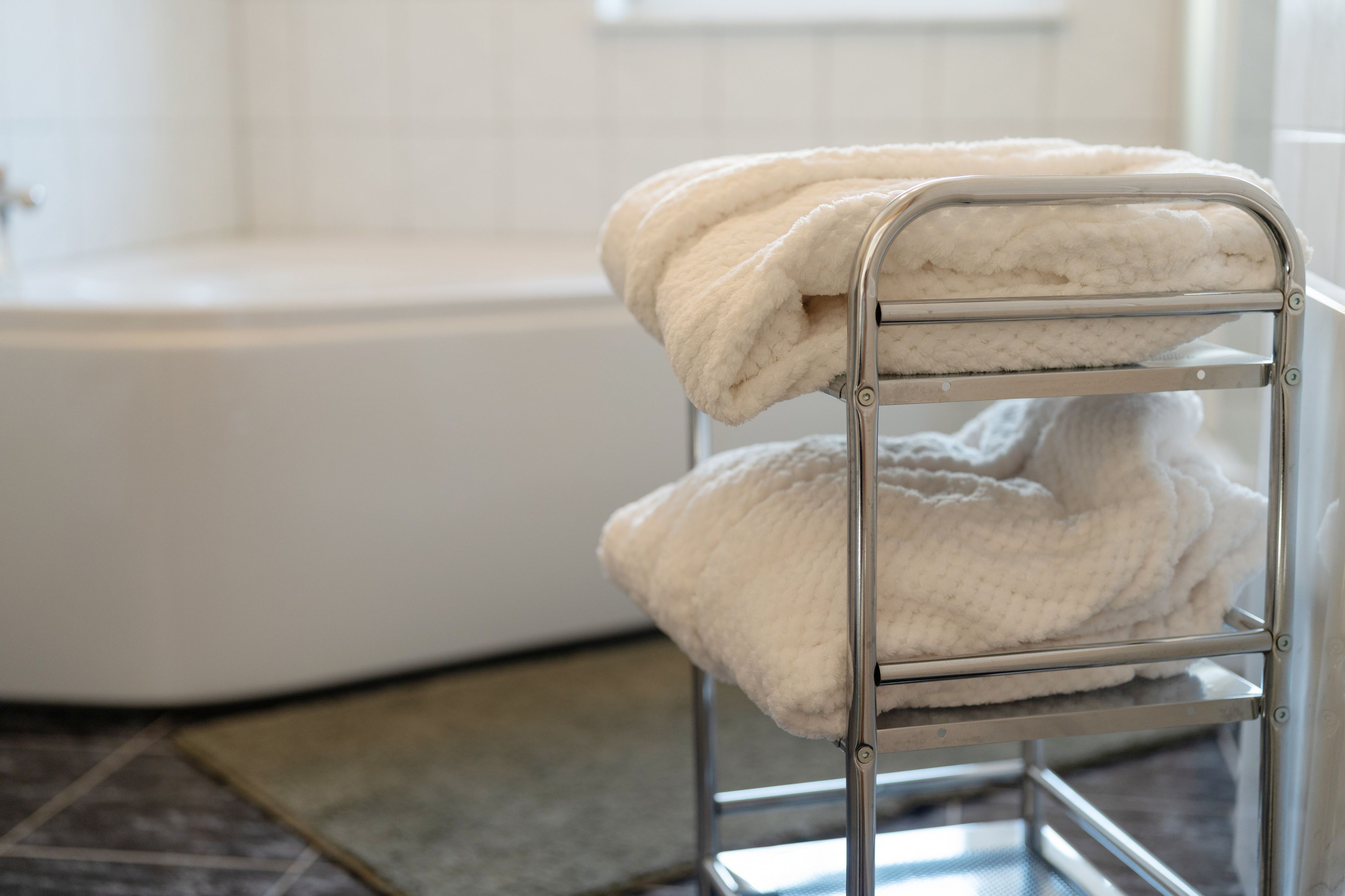 A metal drying rack with two white towels in a bathroom with a white bathtub.