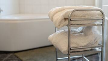 A metal drying rack with two white towels in a bathroom with a white bathtub.