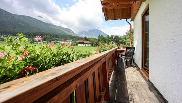 Un balcon doté d’une balustrade en bois, d’où l’on peut admirer un paysage verdoyant avec des montagnes à l’horizon.