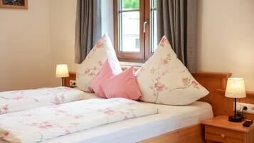 A double bed with floral bedding, two bedside lamps, and a window with curtains.