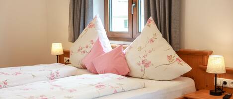 A double bed with floral bedding, two bedside lamps, and a window with curtains.