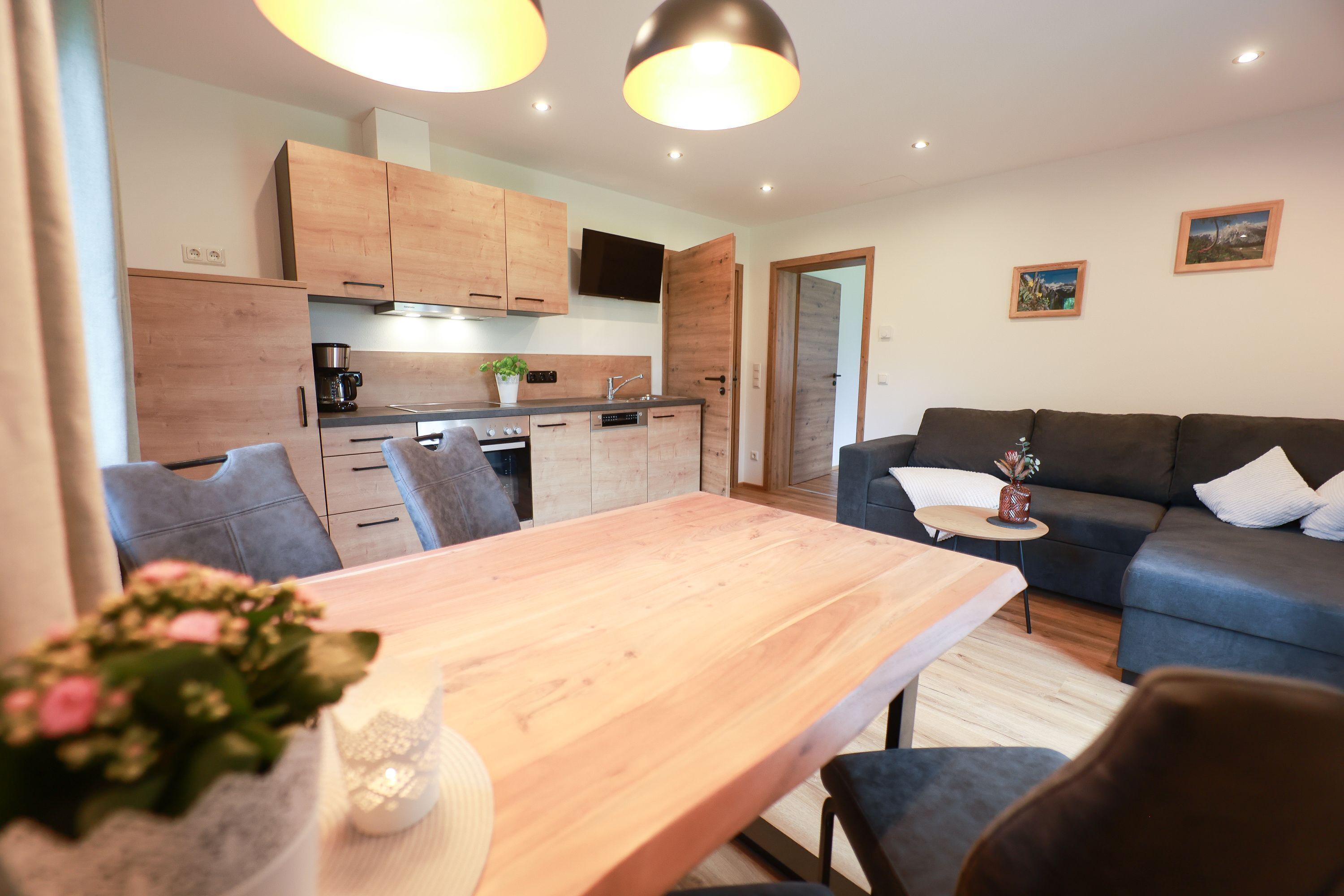 Un espacio habitable moderno con una mesa de comedor de madera, un sofá azul y una zona de cocina con armarios de madera y un horno empotrado.