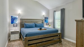 Una camera da letto con un letto in legno, due comodini, una panca da notte, una finestra con tende e opere d'arte alle pareti.