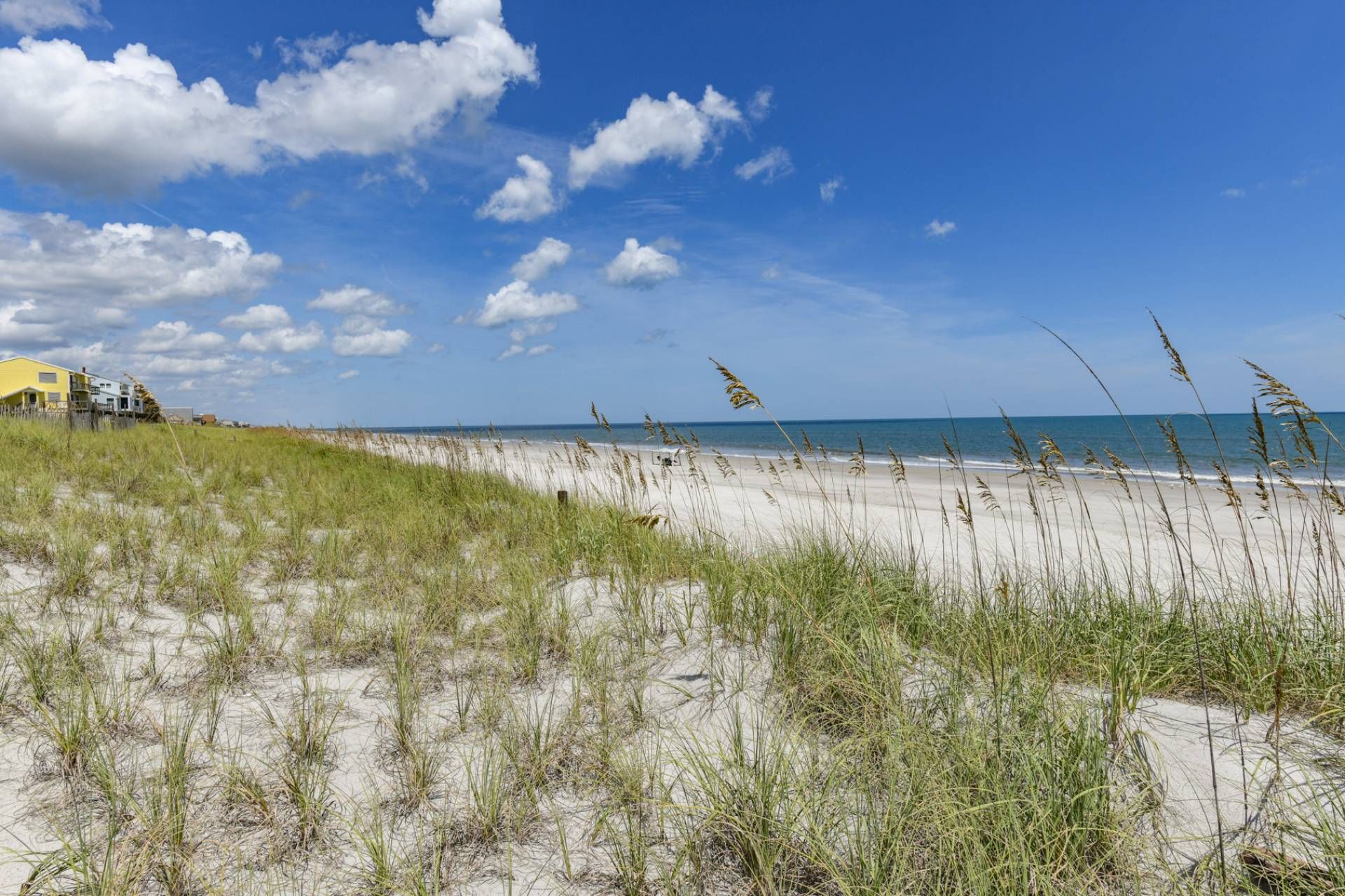 Ein Strand mit Dünen und einem Gebäude im Hintergrund.