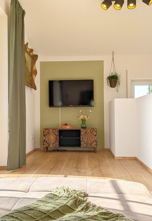 Ein Wohnzimmer mit einem an einer grünen Wand montierten Flachbildfernseher, einem Holzschrank darunter und einem grünen Vorhang links.