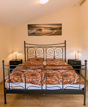Ein Bett mit gemustertem Bettbezug, zwei Nachttische mit Lampen und ein Gemälde an der Wand.