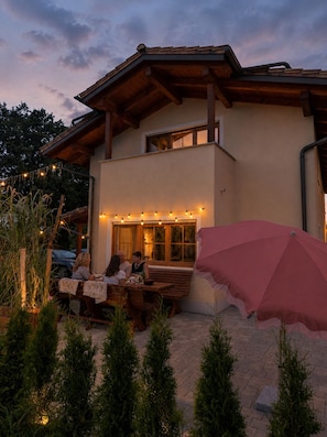 Ein Gebäude mit einer Terrassenfläche, Holzbanken und Lichterketten.