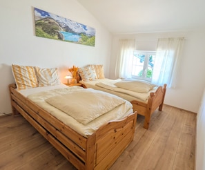 A bedroom with two wooden beds, a nightstand with a lamp, and a painting on the wall. - 2-Bedroom Vacation Rental with a Balcony (Saaldorf-Surheim)