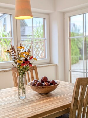 Ein Esstisch mit einer klaren Vase voller Blumen und einer Obstschüssel.