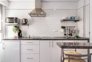 Eine moderne Küche mit weißen Schränken, einer Edelstahl-Dunstesse, einer Mikrowelle und einer Kaffeemaschine.