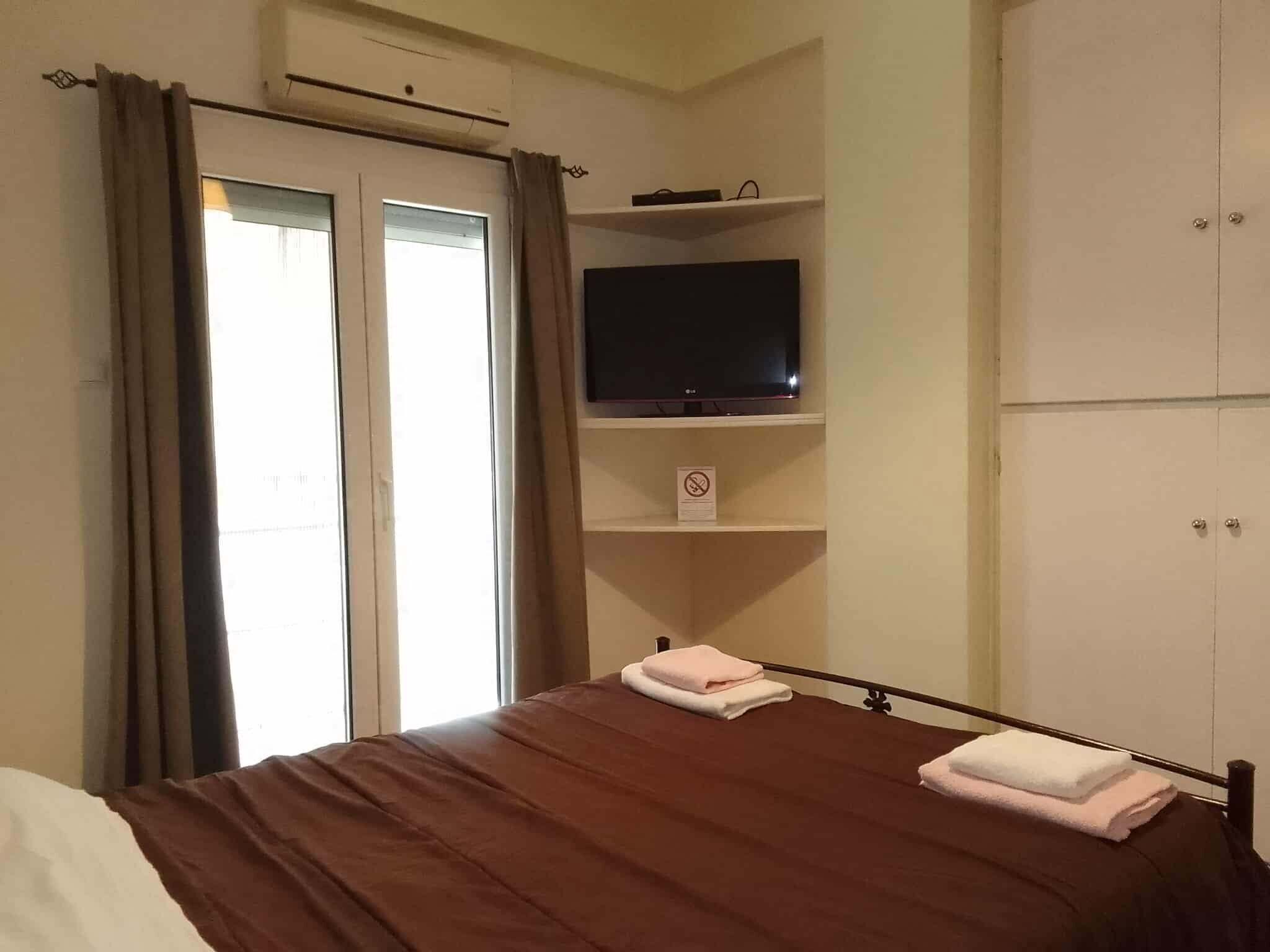 Une chambre d’hôtel avec un lit, un téléviseur posé sur une étagère, une armoire et une fenêtre avec des rideaux.