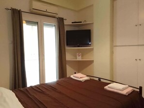 A hotel room with a bed, a television on a shelf, a wardrobe, and a window with curtains. - Athens HOME 2 (Athina)