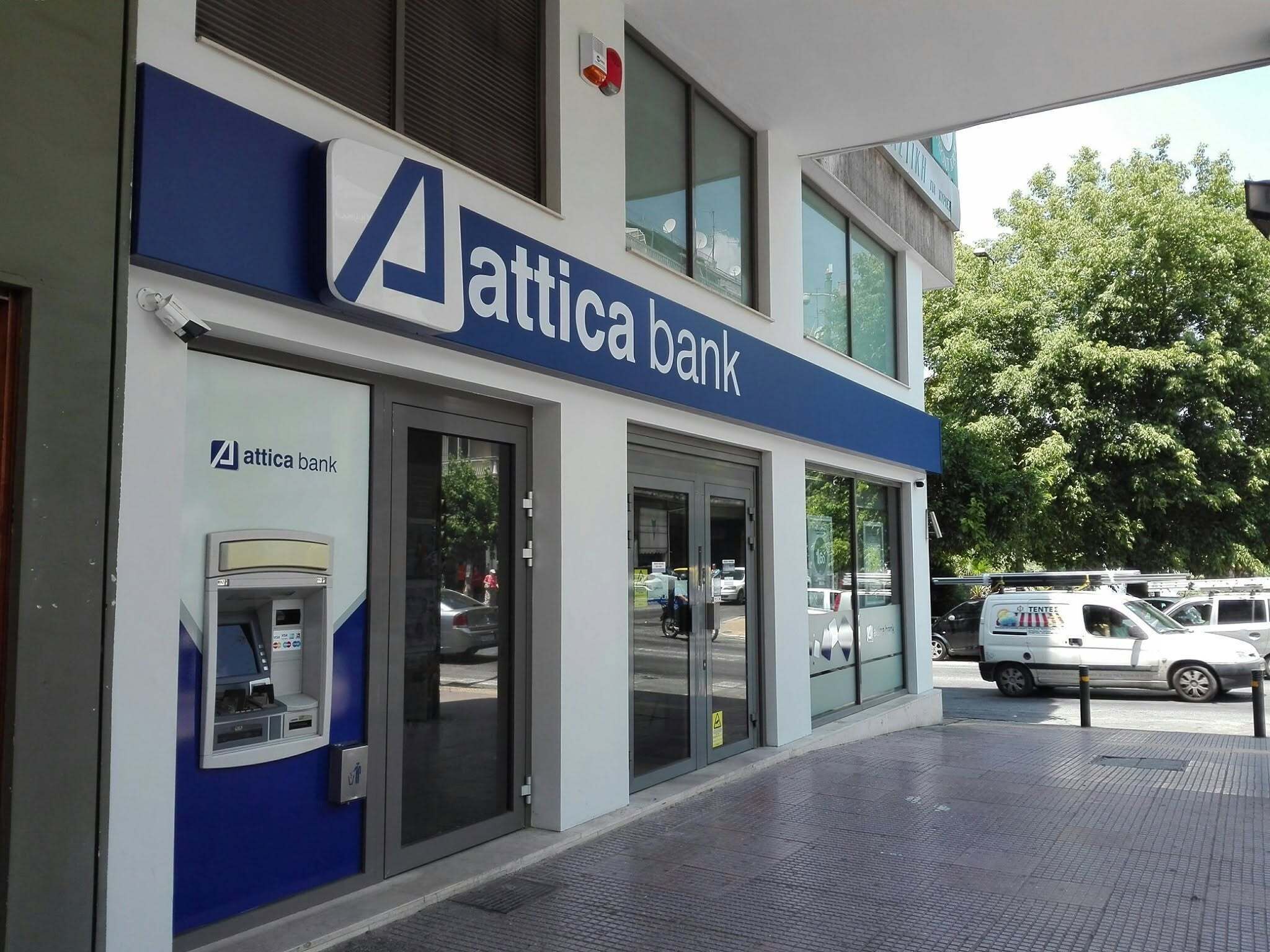 An attica bank building with a blue and white facade, a glass entrance, and a visible ATM on the ground floor.