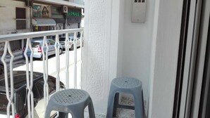 A balcony with two plastic stools, a railing, and a view of parked cars and buildings. - Athens HOME 2 (Athina)