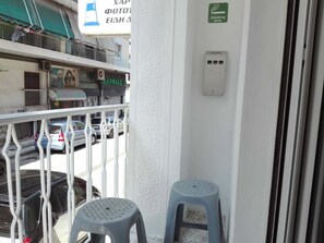 Ein Balkon mit zwei Plastik Hockern, einer Brüstung und Blick auf geparkte Autos und Gebäude.