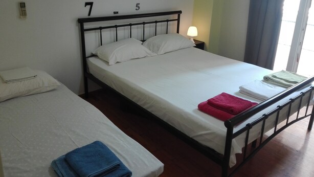 A hotel room with two beds, a nightstand with a lamp, and a window with curtains. - Athens HOME 2 (Athina)