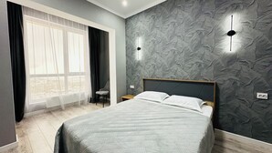 Un dormitorio moderno con una cama grande, una silla, un ventanal con cortinas y una pared texturizada.