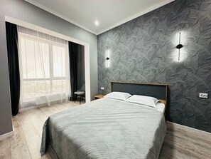 A modern bedroom with a large bed, a chair, a window with curtains, and a textured wall. - Loft Apartment near MEGA Alma-Ata (Almaty)