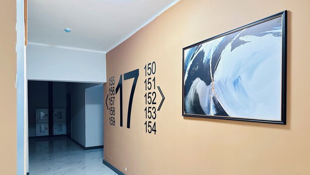 Un pasillo con el número 17 grande en la pared, un cuadro abstracto enmarcado y una puerta que da a una habitación con piso de baldosas.
