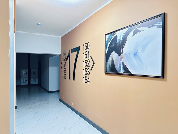 A hallway with a large number '17' on the wall, a framed abstract painting, and a door leading to a room with a tiled floor. - Loft Apartment near MEGA Alma-Ata (Almaty)