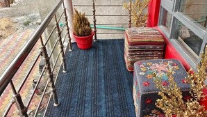 Un balcón con baranda de metal, una planta en maceta, un tapete estampado y cojines apilados.