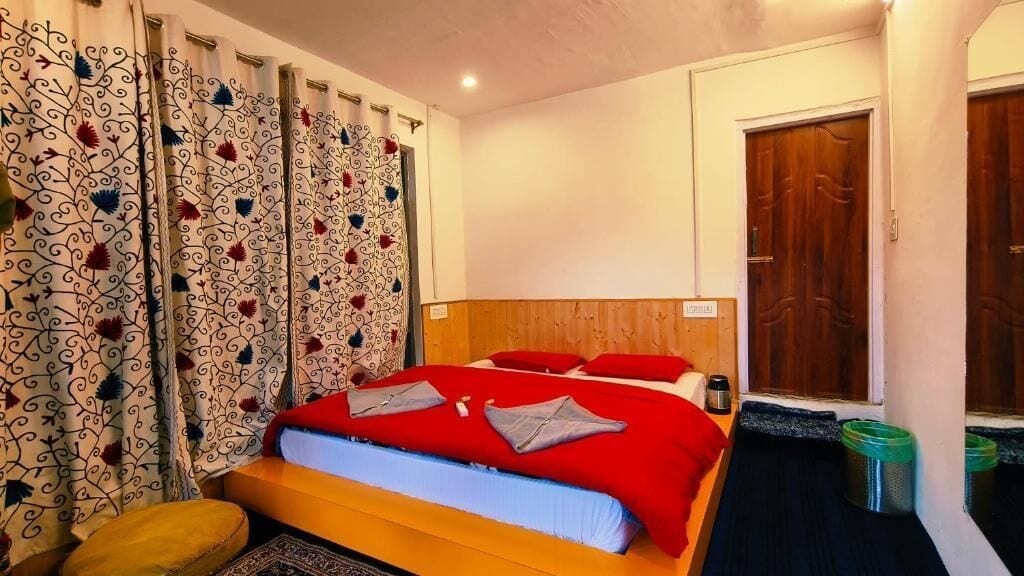 Habitación de hotel con cama, cortinas, cabecero de madera, mesita de noche y puerta.