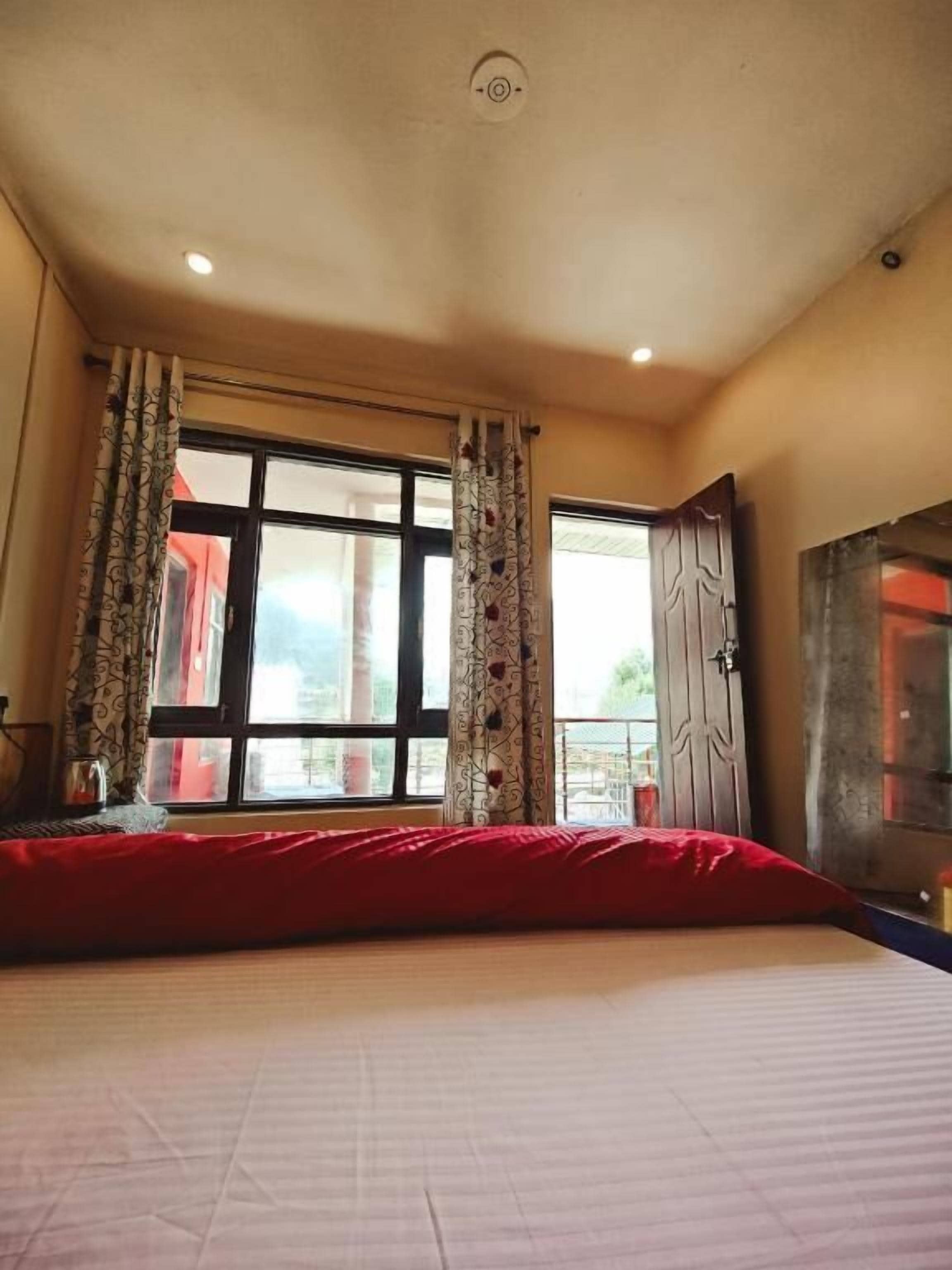 A bedroom with a large bed, a window with curtains, and a door leading to a balcony.
