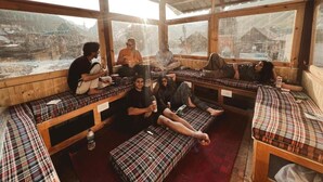 Un grupo de personas sentadas en bancos de estampado escocés en una habitación con ventanas amplias que dan a un paisaje montañoso.