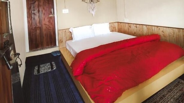 Habitación de hotel con una cama, una puerta de madera, una lámpara fijada a la pared y un tapete estampado.