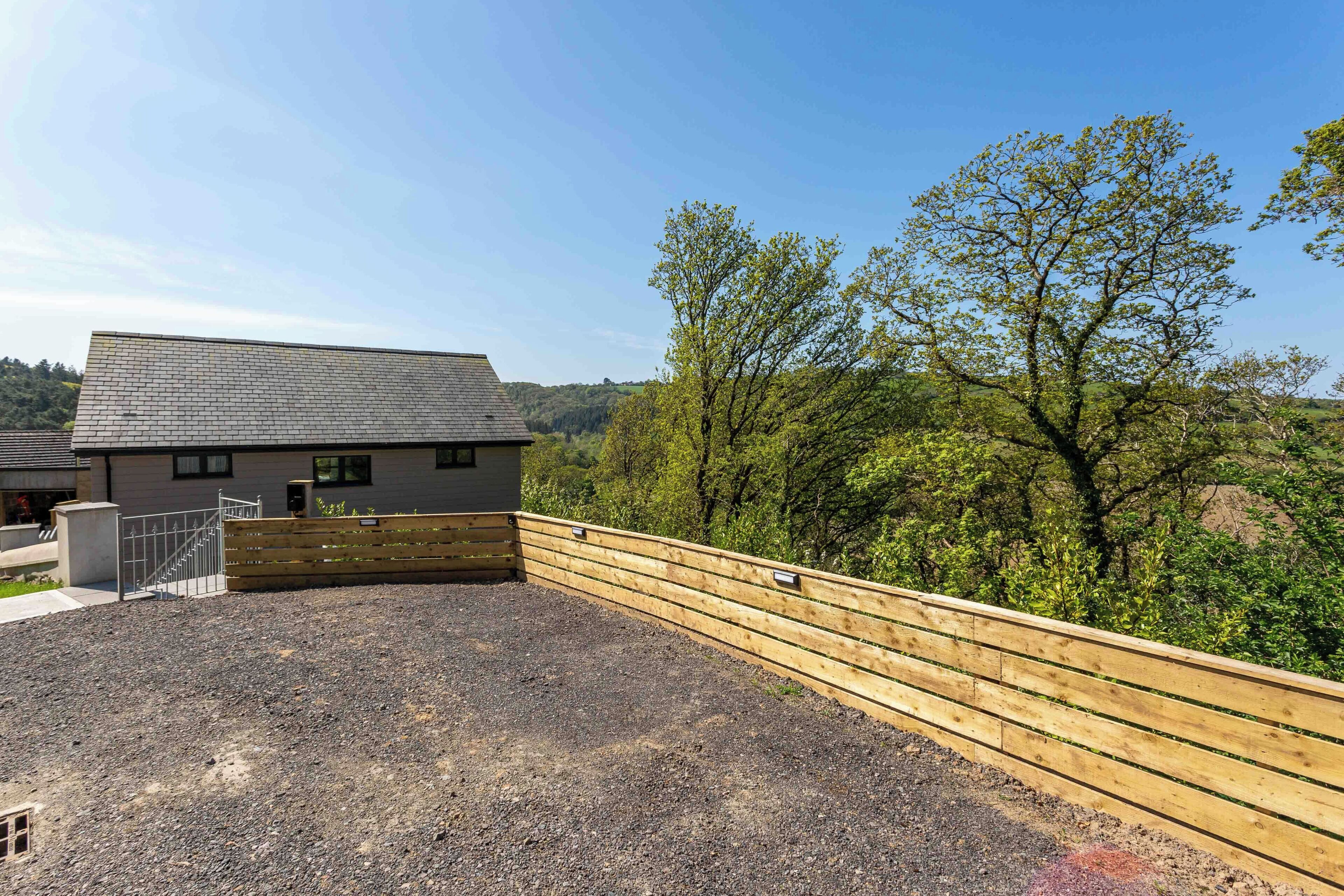A building with a sloped roof, a gravel driveway, and a wooden fence.