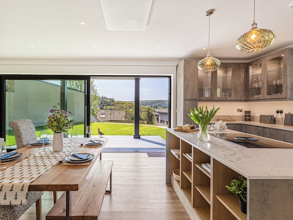 A modern kitchen with a large island, wooden flooring, and a view of the outdoors.