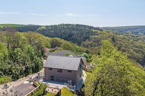 A modern two-story building with a flat roof, surrounded by lush greenery and hills.