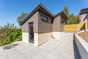 A modern house with a sloped roof, a front door, and a small set of stairs leading to a wooden deck.