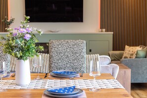 A dining area with a table set for two, a vase with flowers, and a television in the background.