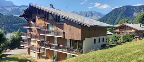 Un chalet de varios pisos con balcones, frente a un paisaje montañoso.