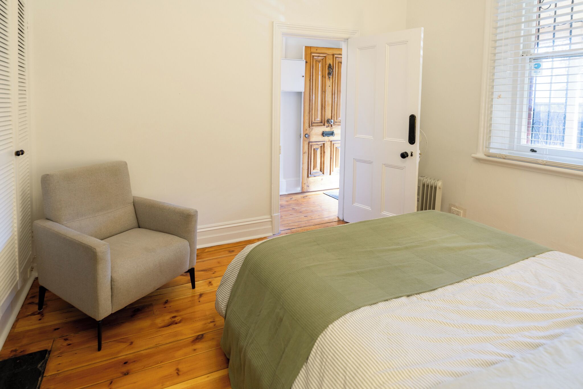 A bedroom with a bed, a chair, a radiator, and a door leading to another room.