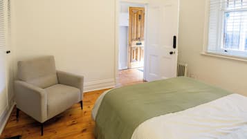 A bedroom with a bed, a chair, a radiator, and a door leading to another room.