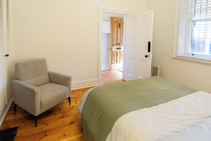 A bedroom with a bed, a chair, a radiator, and a door leading to another room.