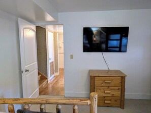Une pièce avec une commode en bois, un téléviseur fixé au mur et une porte donnant sur une autre pièce.