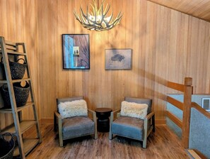 Ein gemütliches Zimmer mit Holzwänden, zwei Sessel mit weichen Kissen, einem kleinen runden Tisch und einer Chandelier.