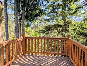 Une terrasse en bois dotée d’une rambarde, entourée de grands arbres et avec une chaîne de montagnes en arrière-plan.