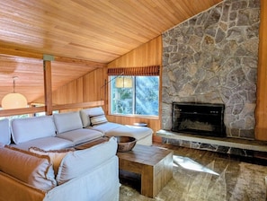 Ein gemütliches Wohnzimmer mit Kamin aus Stein, Holzboden und einem großen Fenster.