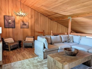 Ein gemütliches Zimmer mit Holzboden, einem hellen Sofa, einem Holztisch und gerahmten Bildern an der Wand.