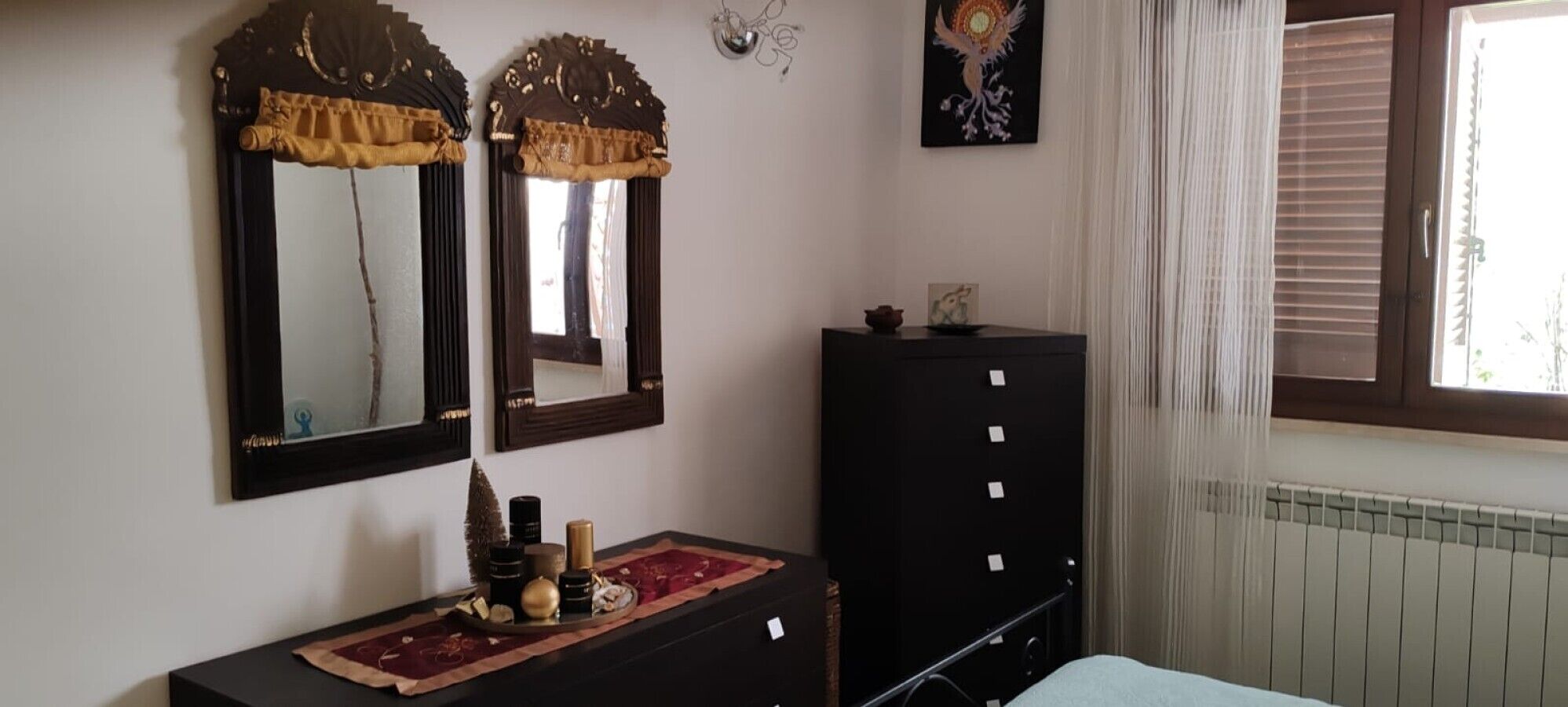 Ein Zimmer mit zwei Spiegeln, einem Schminktisch, einer Heizung und einem Fenster mit Jalousien.
