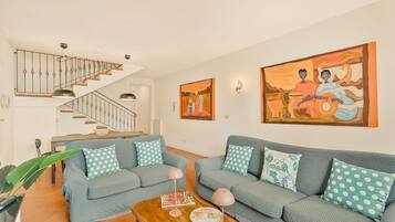 Un salon avec un escalier, un ensemble de meubles pour le salon et un tableau accroché au mur.