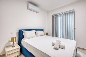 A hotel room with a bed, a bedside table with a lamp, and an air conditioning unit. - Beautiful, fully equipped 3BR in Sliema w/Balcony (Tas-Sliema)